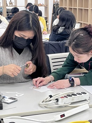 學生專注焊接迴紋針與LED的手部特寫圖片