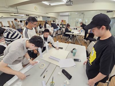 學生動手摺紙、黏貼膠帶製作軌道的特寫，展現「先做再說」的動手精神圖片